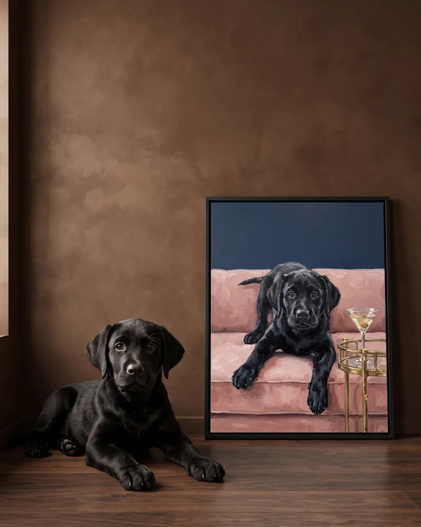 Bear, a black Labrador retriever puppy, beside a black framed canvas of their own Olive & Velvet portrait.