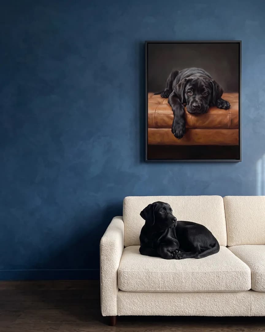 Bear, un chiot labrador noir, à côté d'une toile encadrée noire de son portrait Repos de velours.